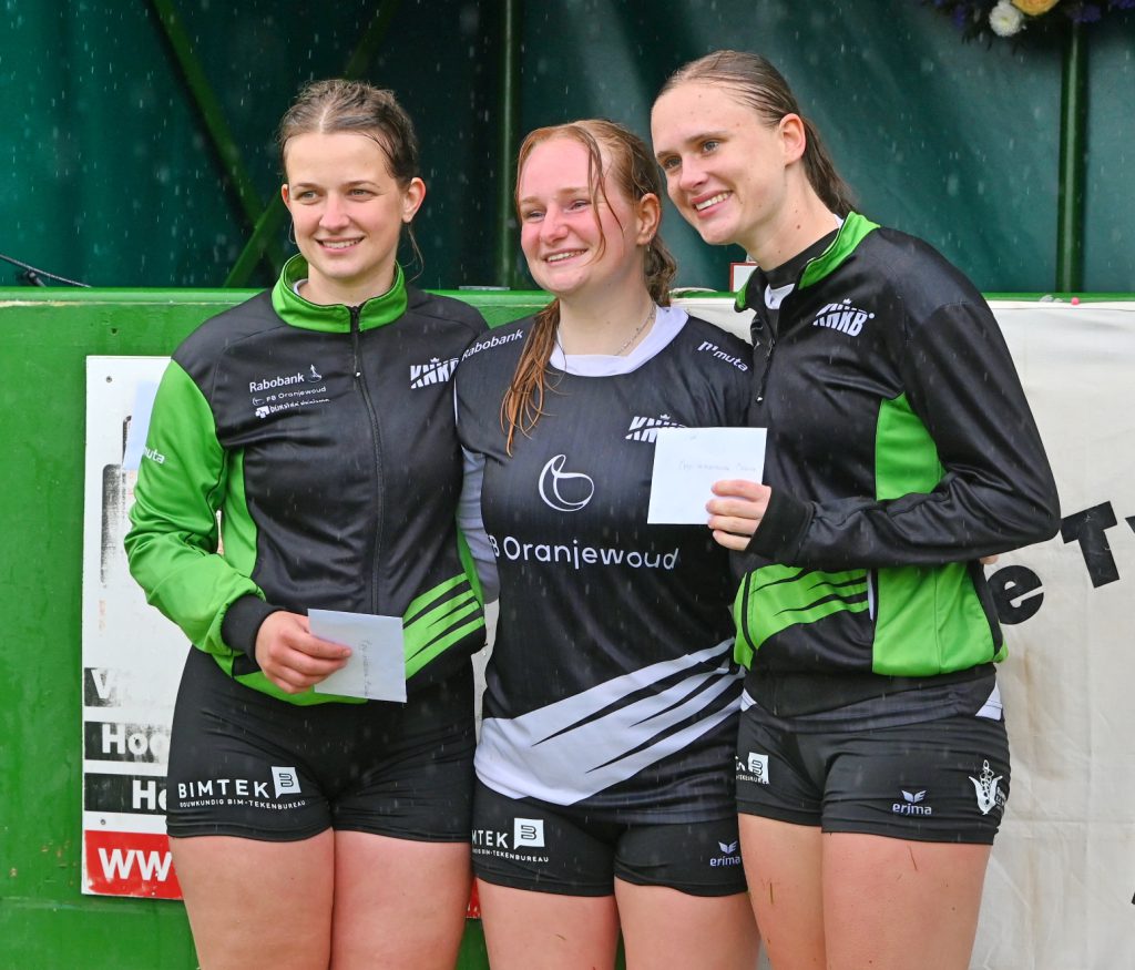 1ste Prijs Herkansing Dames 1ste Klas - kaatsnieuws.com Three smiling female athletes in black-and-green uniforms pose together, each holding a note card after a race.
