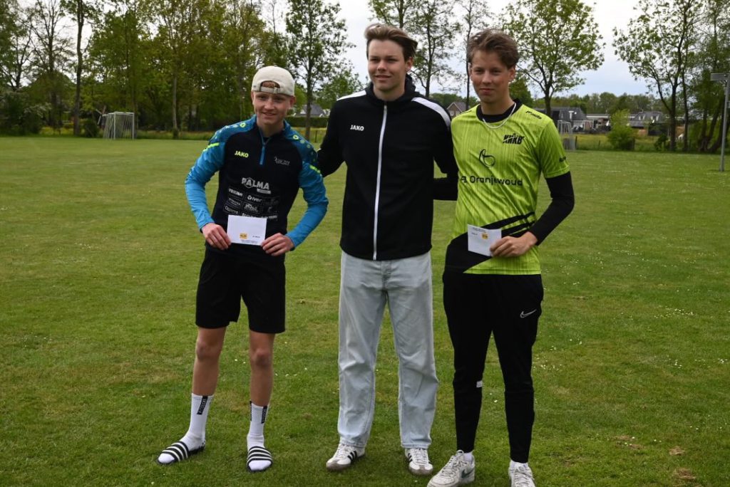 Broeksterwald 2 - kaatsnieuws.com Three young men stand on a grassy field posing with certificates after a sports event, smiling at the camera.
