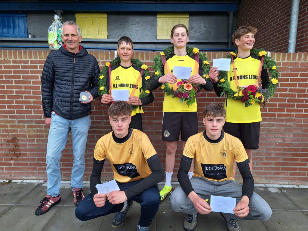 Jongens Holwert - kaatsnieuws.com Youth soccer team posing for a photo with coach, some players holding envelopes and wearing flower wreaths and medals.