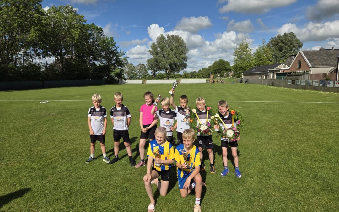 Youth soccer team posing on a sunlit field with trophies and flowers, smiling after a win.