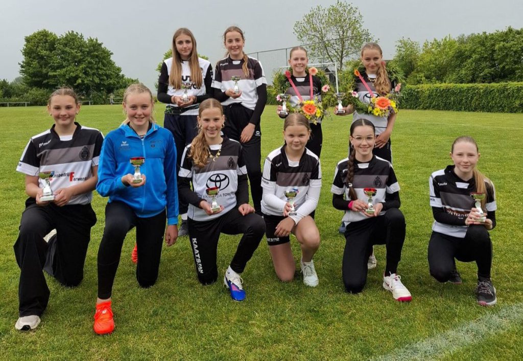 b pup - kaatsnieuws.com Group of young female soccer players posing on a grassy field with trophies and flower bouquets.