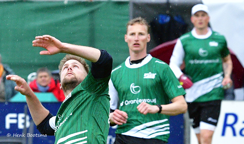Player in a green jersey reaches upward during a team match, with two teammates in the background watching.
